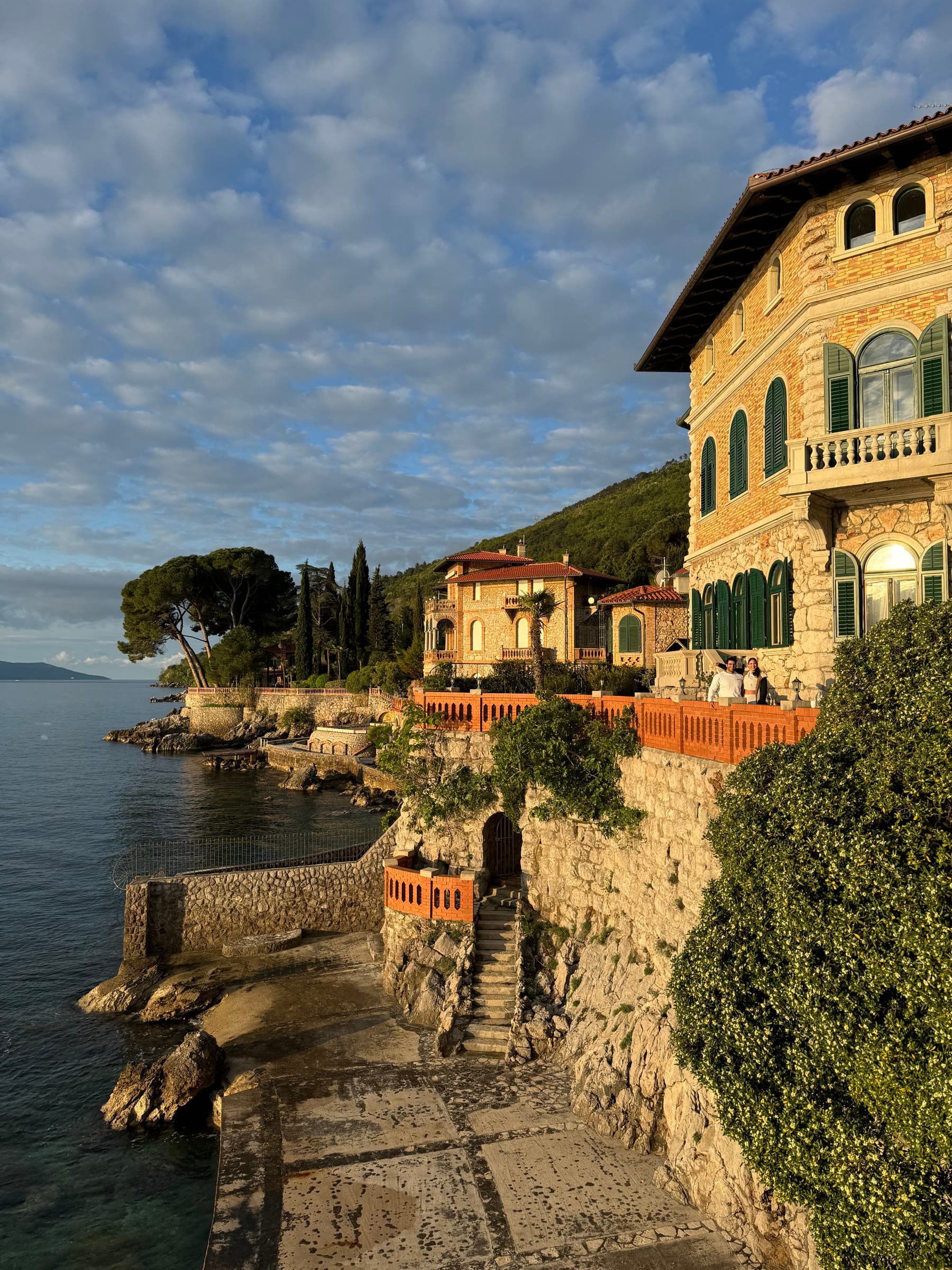 A stone villa with green shutters and a terracotta terrace on a rocky cliff above the sea