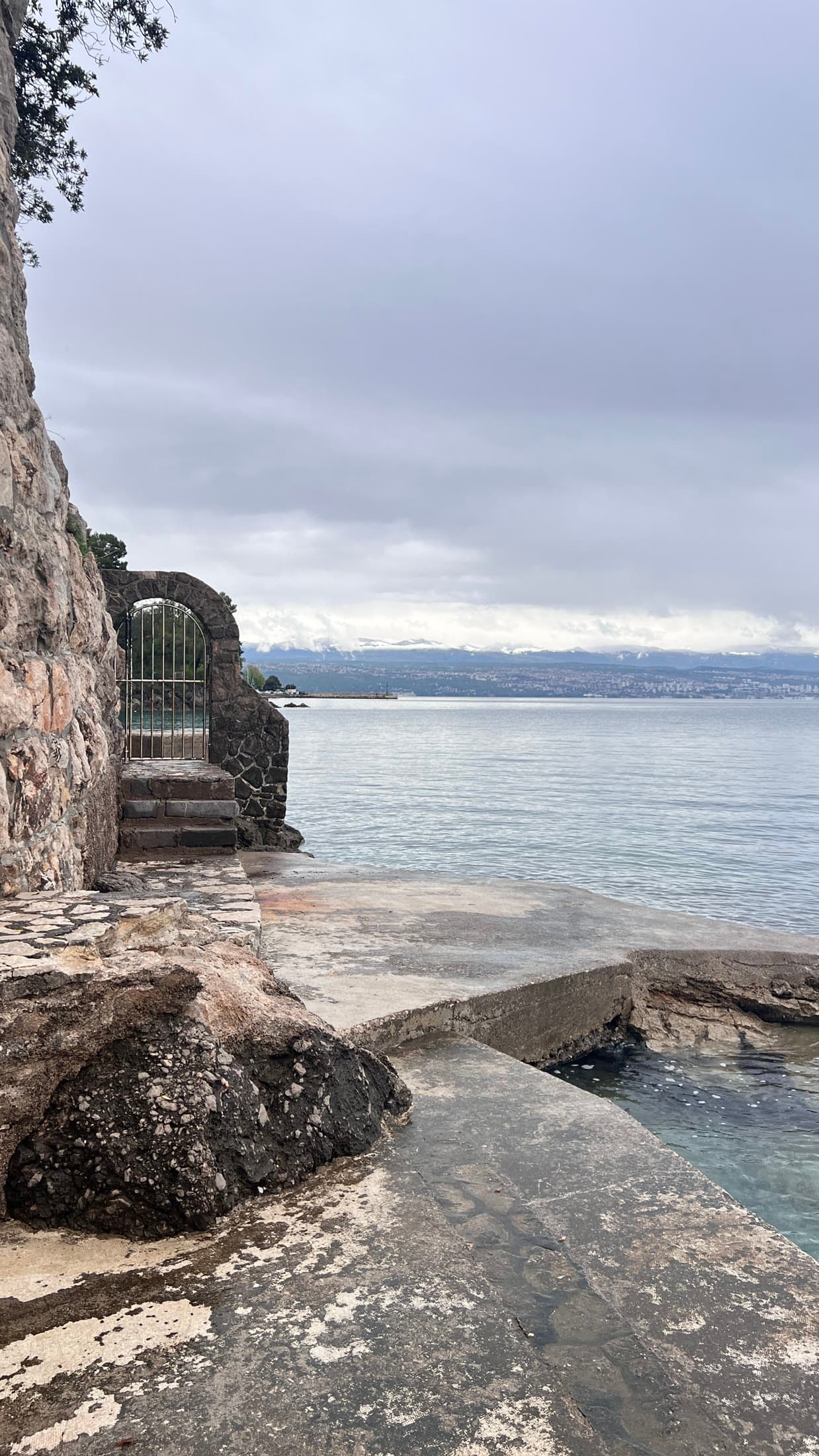 A weathered stone landing at the water’s edge with a small arched gate set into the cliff