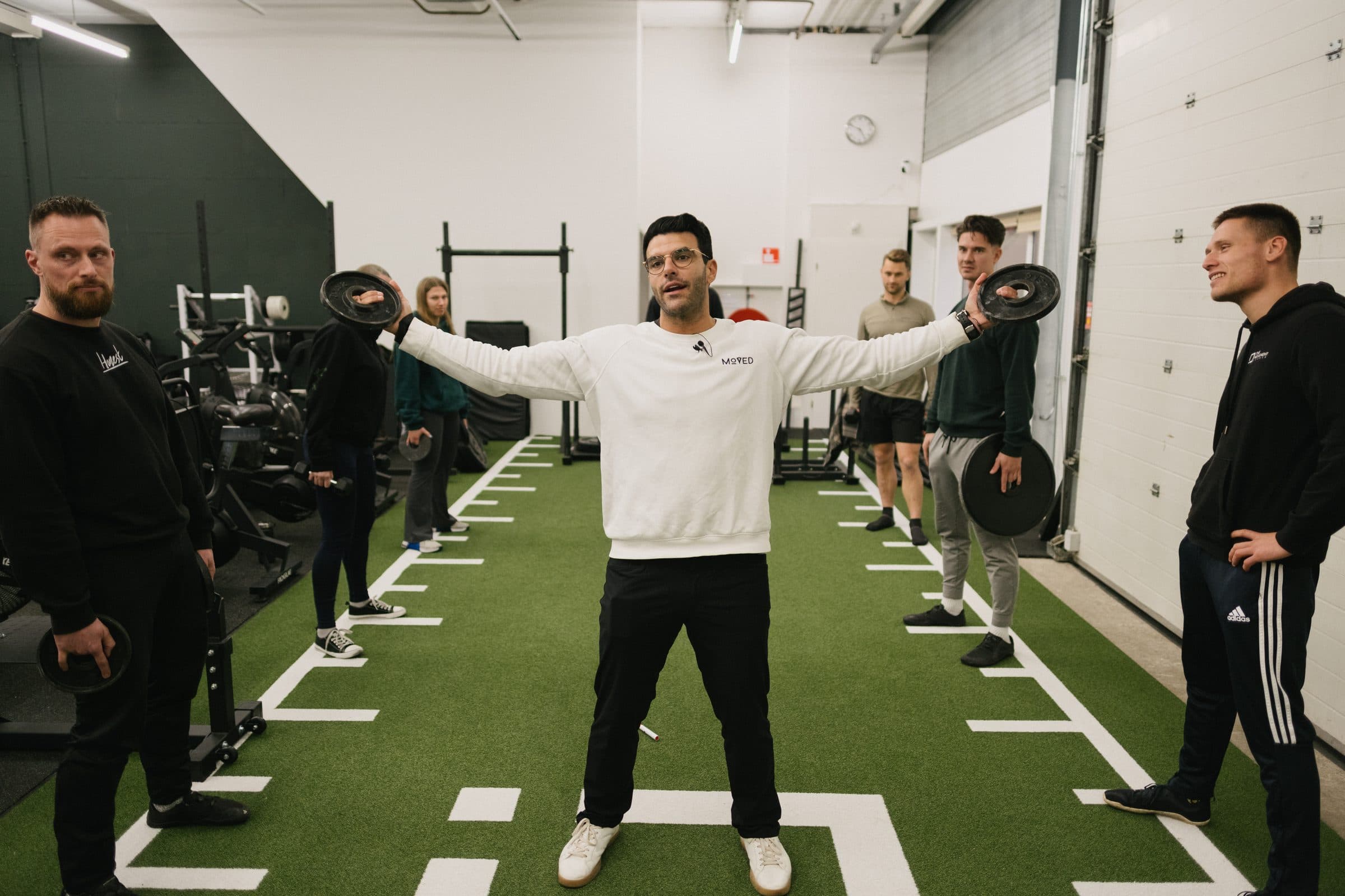 Richard Aceves standing arms outstretched, coaches mirroring the position around him