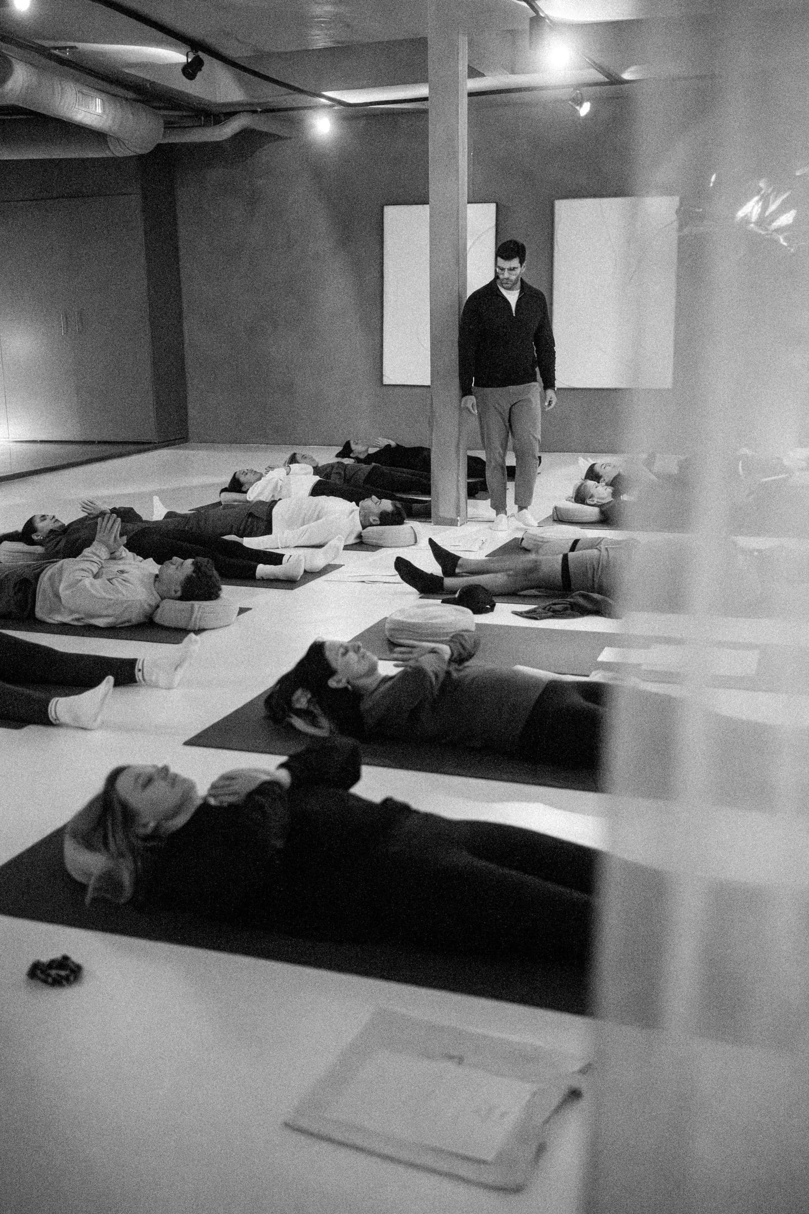 A group lying down on mats during a guided breathwork session, Richard standing above