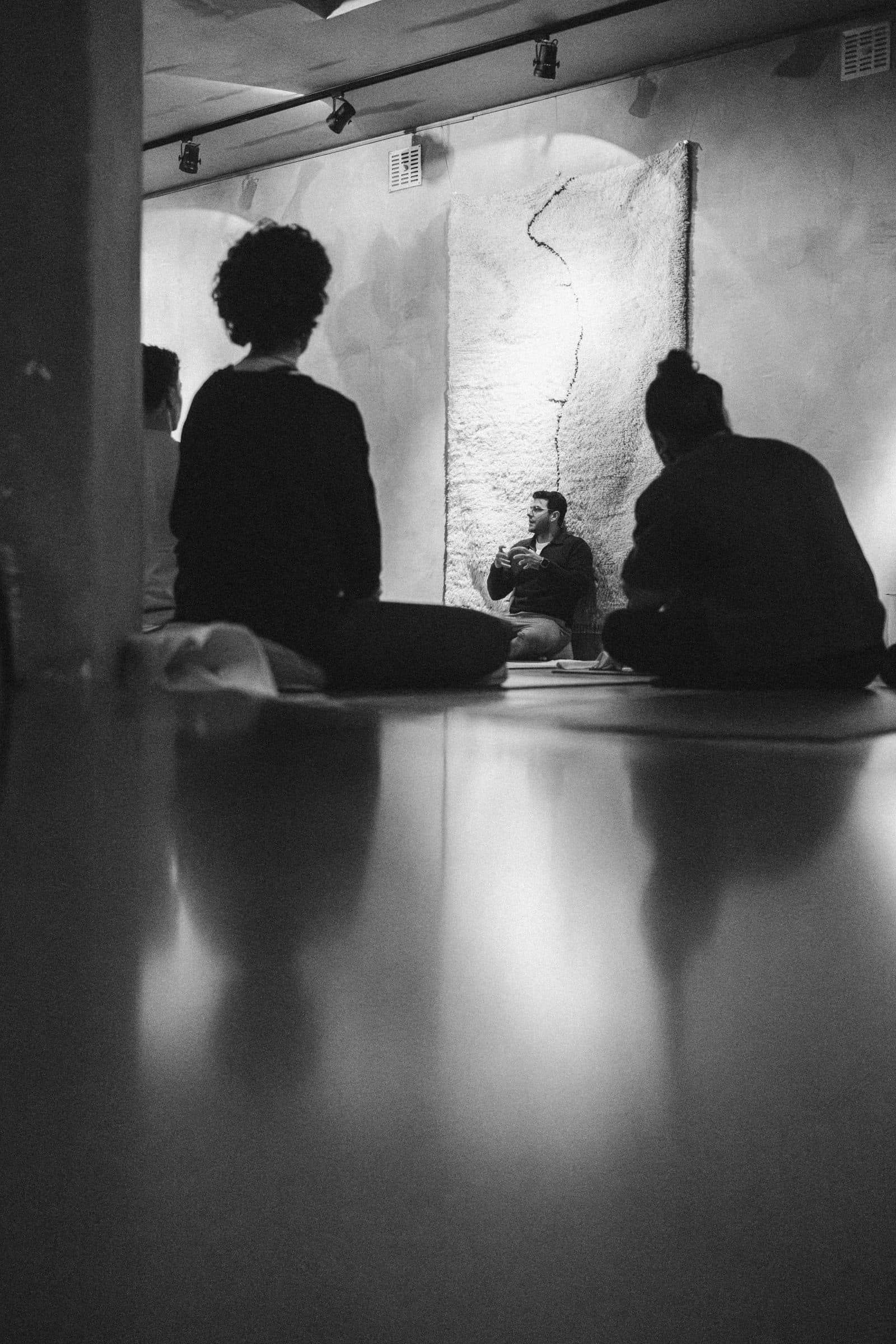 Silhouetted figures reflected on a dark floor during a breathwork session