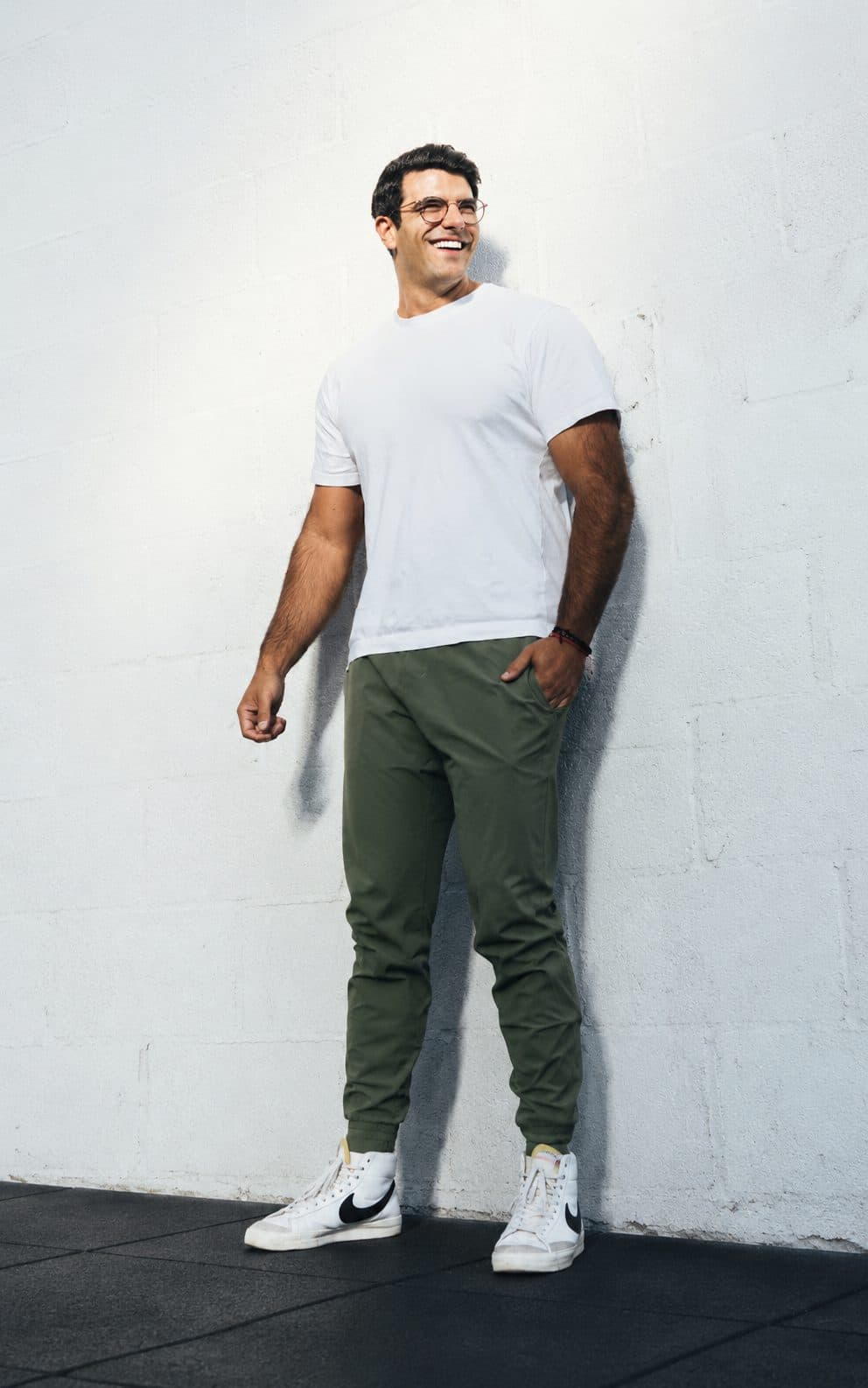Richard Aceves standing relaxed against a white wall, mid-laugh