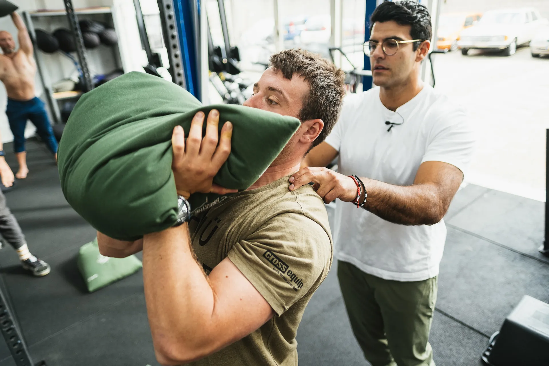 Richard Aceves coaching a client through a sandbag carry, hand on the upper back to cue tension