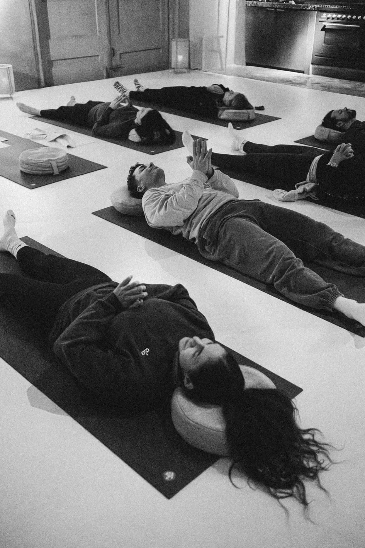 Several people lying on mats in a bright room, hands resting on the body, during a guided floor practice